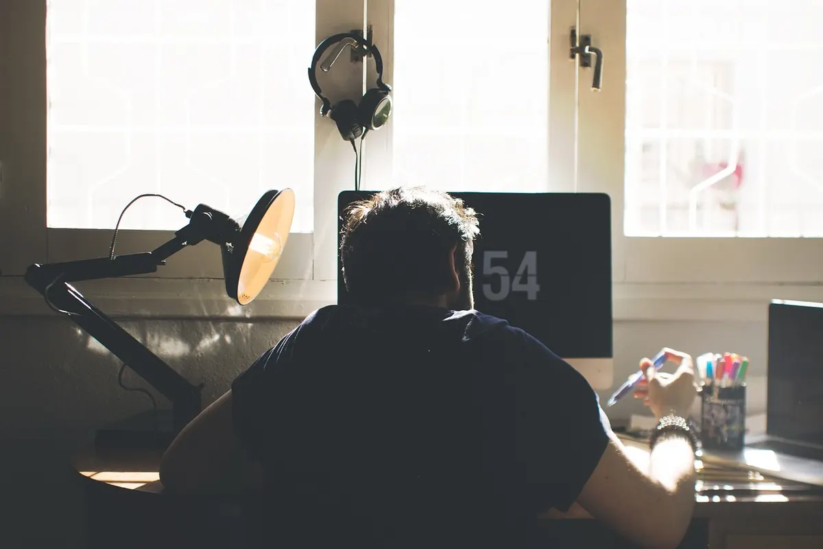 Vue de dos d’une personne assise à son bureau devant un écran, dans une pièce éclairée par une fenêtre